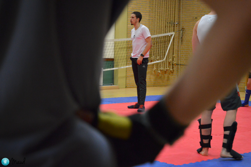 Kickbokstrainer geeft instructies tijdens een groepsles terwijl deelnemers trainen op de mat