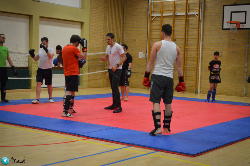 Groep deelnemers volgt een kickbokstraining en oefent sparren op de mat in een sportschool