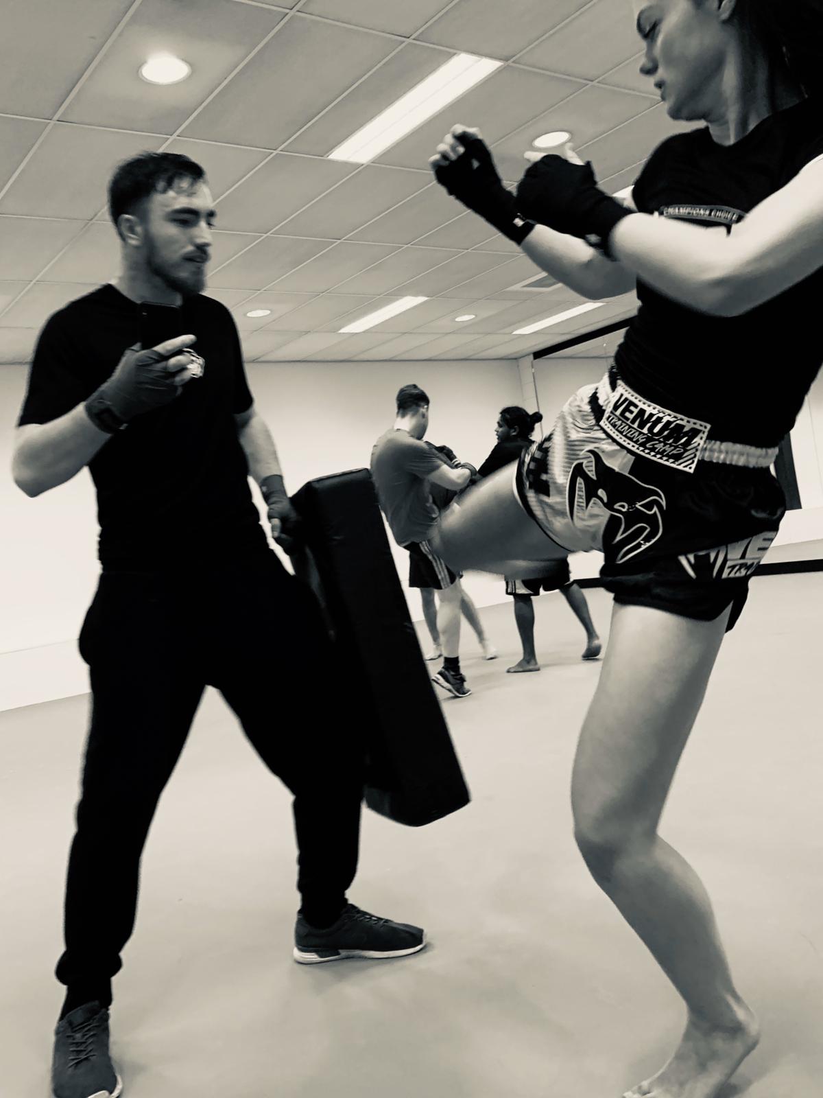 Deelnemer oefent een trap op een stootkussen tijdens een kickbokstraining in een groepsles