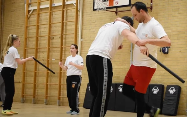 Deelnemers oefenen Krav Maga wapenverdediging tegen een stok tijdens een groepsles zelfverdediging