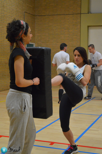 Vrouw oefent een trap tijdens een zelfverdedigingstraining met stootkussen en bokshandschoenen